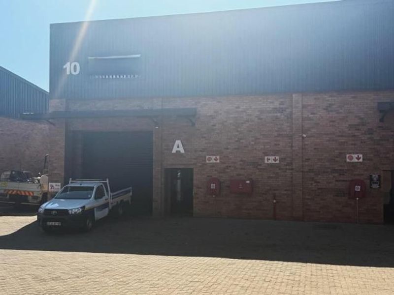 Commercial warehouse unit featuring a brick facade, roller shutter door access, and paved exterior area.