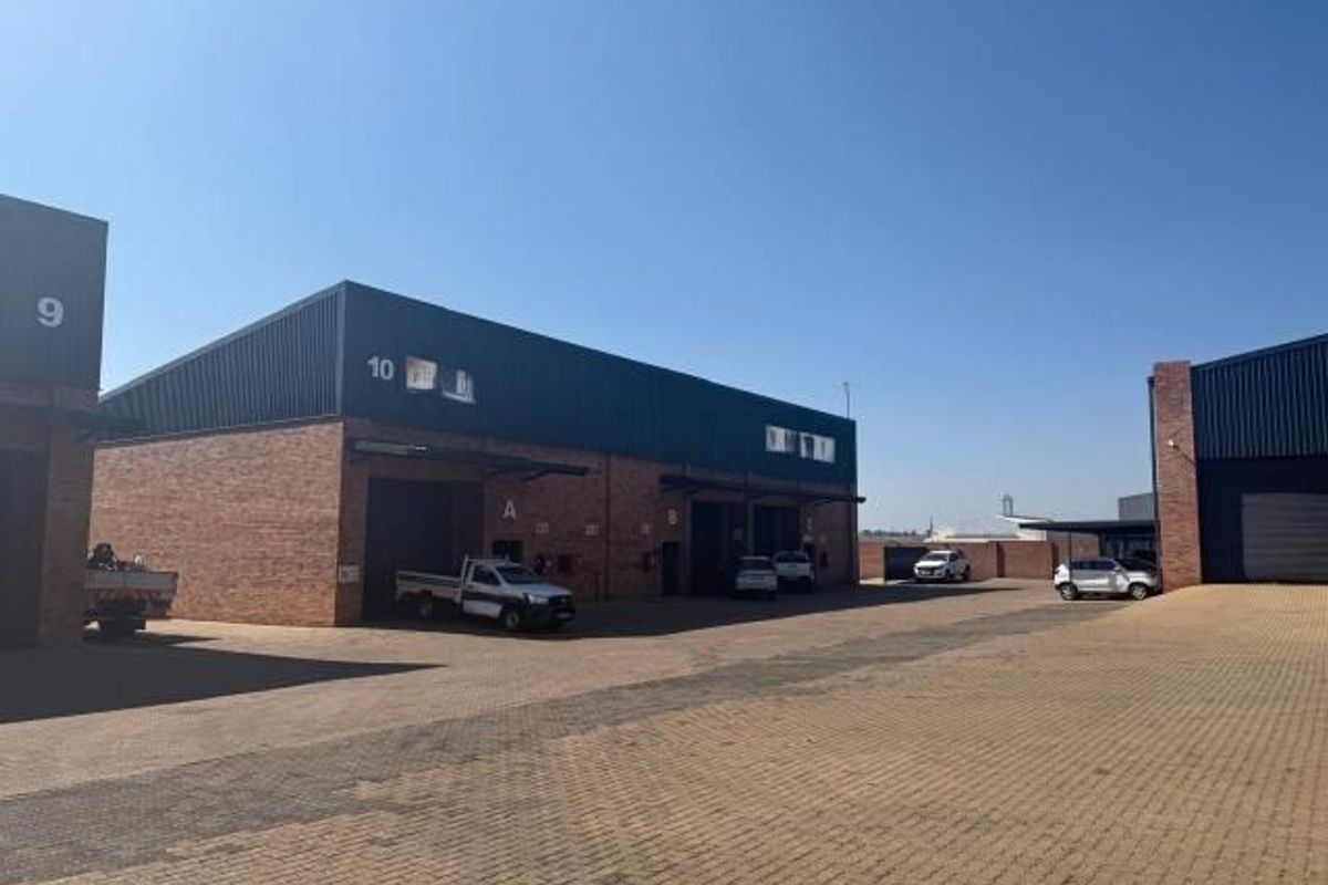 Exterior view of a commercial industrial park featuring brick and metal facade units with roller shutter doors and a paved driveway.