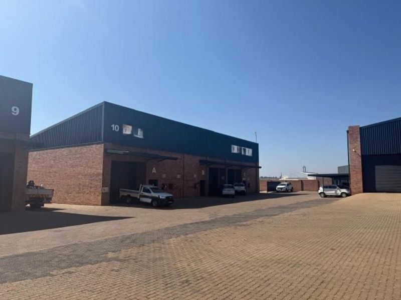 Exterior view of a commercial industrial park featuring brick and metal facade units with roller shutter doors and a paved driveway.