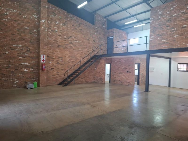 Spacious industrial utility space featuring exposed brick walls, polished concrete flooring, and a mezzanine level accessible via a steel staircase.