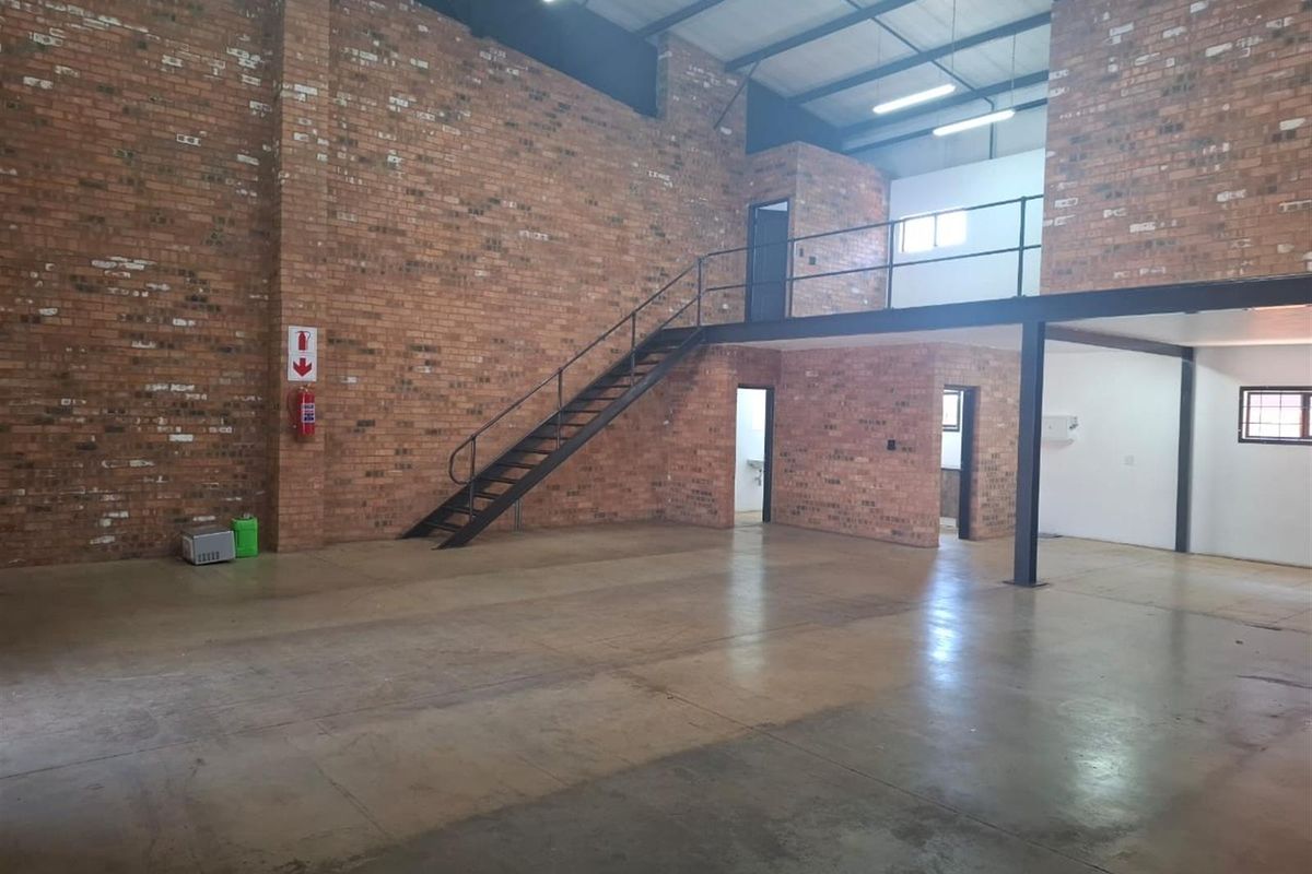 Spacious industrial utility space featuring exposed brick walls, polished concrete flooring, and a mezzanine level accessible via a steel staircase.