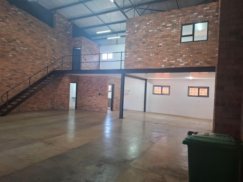 Spacious industrial-style open plan commercial unit featuring exposed brick walls, a mezzanine level with steel staircase, and ample natural light through multiple windows.