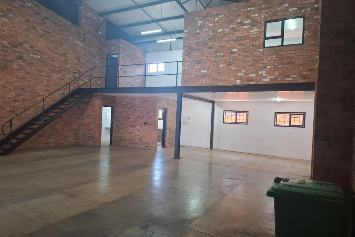 Spacious industrial-style open plan commercial unit featuring exposed brick walls, a mezzanine level with steel staircase, and ample natural light through multiple windows.