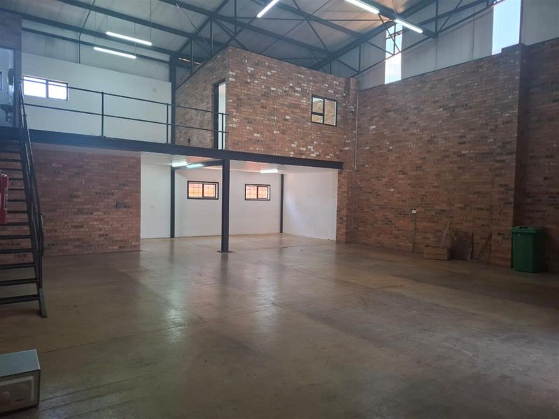 Spacious industrial commercial unit featuring high ceilings with exposed steel trusses, a mezzanine level, concrete flooring, and attractive exposed brickwork.