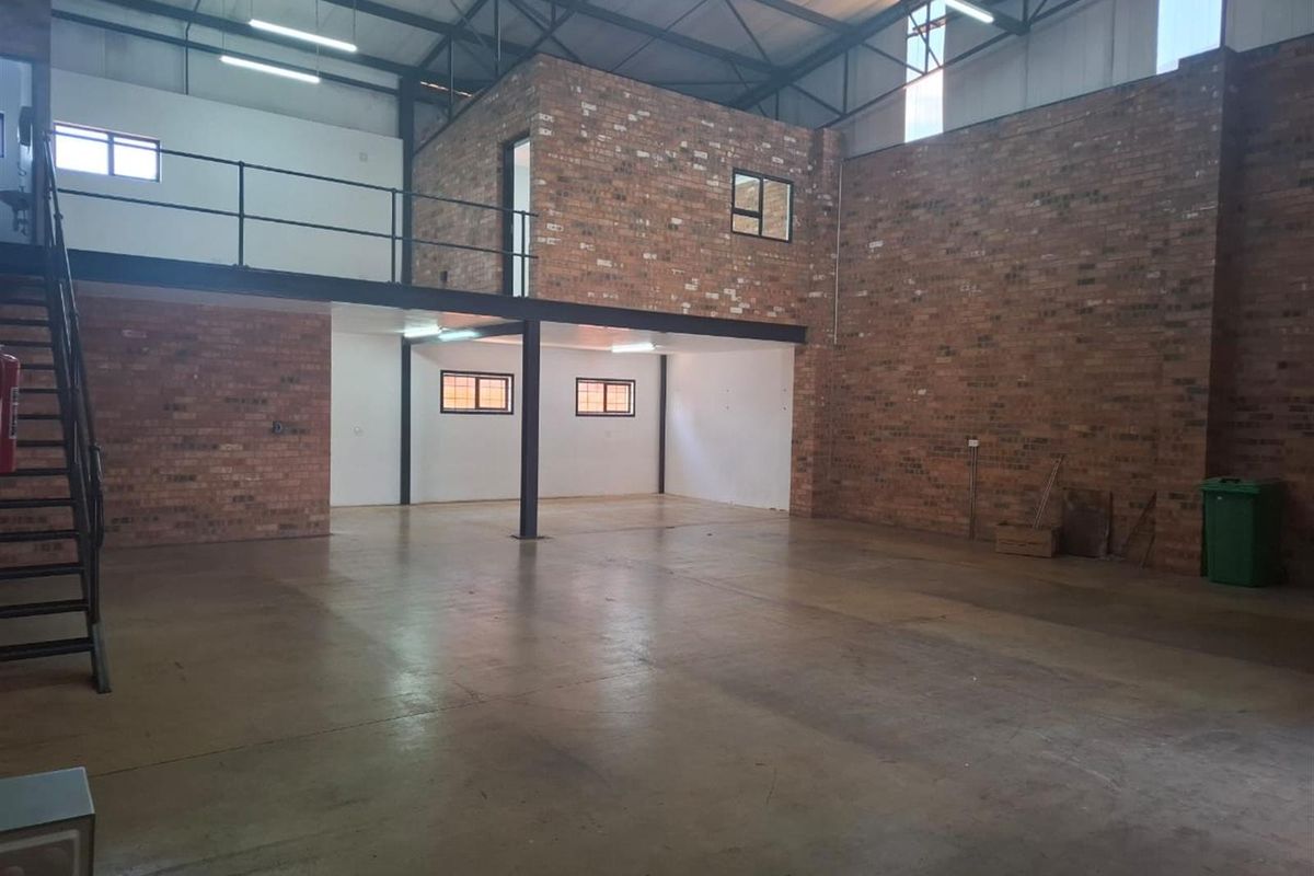 Spacious industrial commercial unit featuring high ceilings with exposed steel trusses, a mezzanine level, concrete flooring, and attractive exposed brickwork.