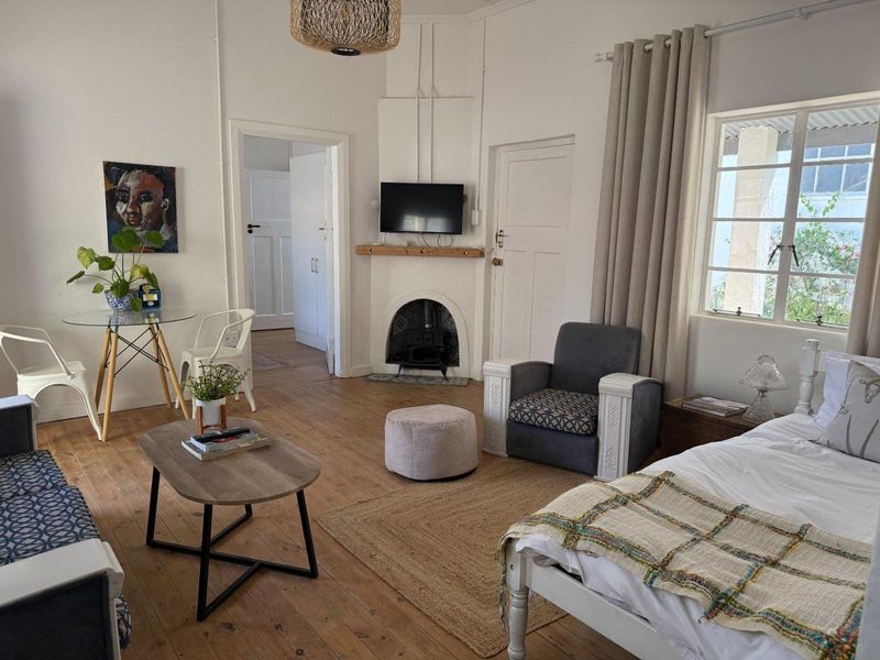A well-lit bedroom featuring original timber flooring, a classic fireplace, and large windows that provide natural light.