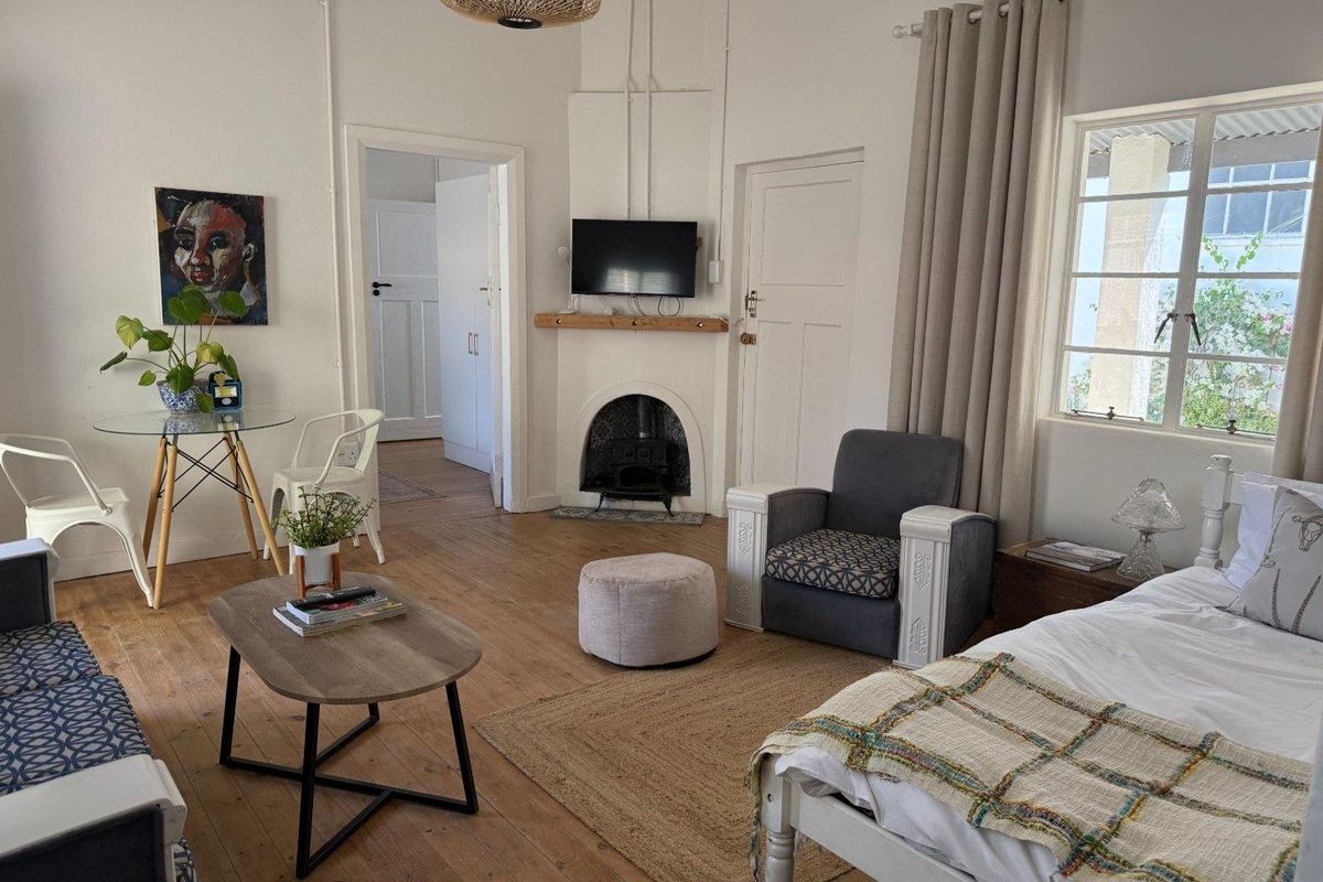 A well-lit bedroom featuring original timber flooring, a classic fireplace, and large windows that provide natural light.