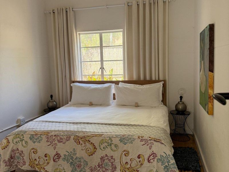 A cozy bedroom featuring timber flooring, a central ceiling light fixture, and a window providing natural light.