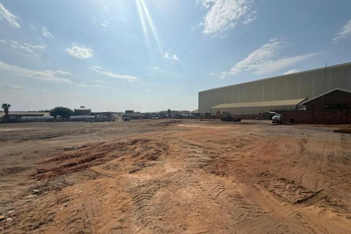 Expansive industrial yard space with unpaved ground, adjacent to a large warehouse structure, offering significant potential for development or heavy-duty storage.