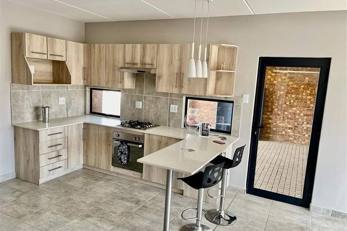 Modern kitchen featuring light wood-grain cabinetry, stone countertops, a built-in oven, gas hob, extractor fan, and a breakfast bar island.