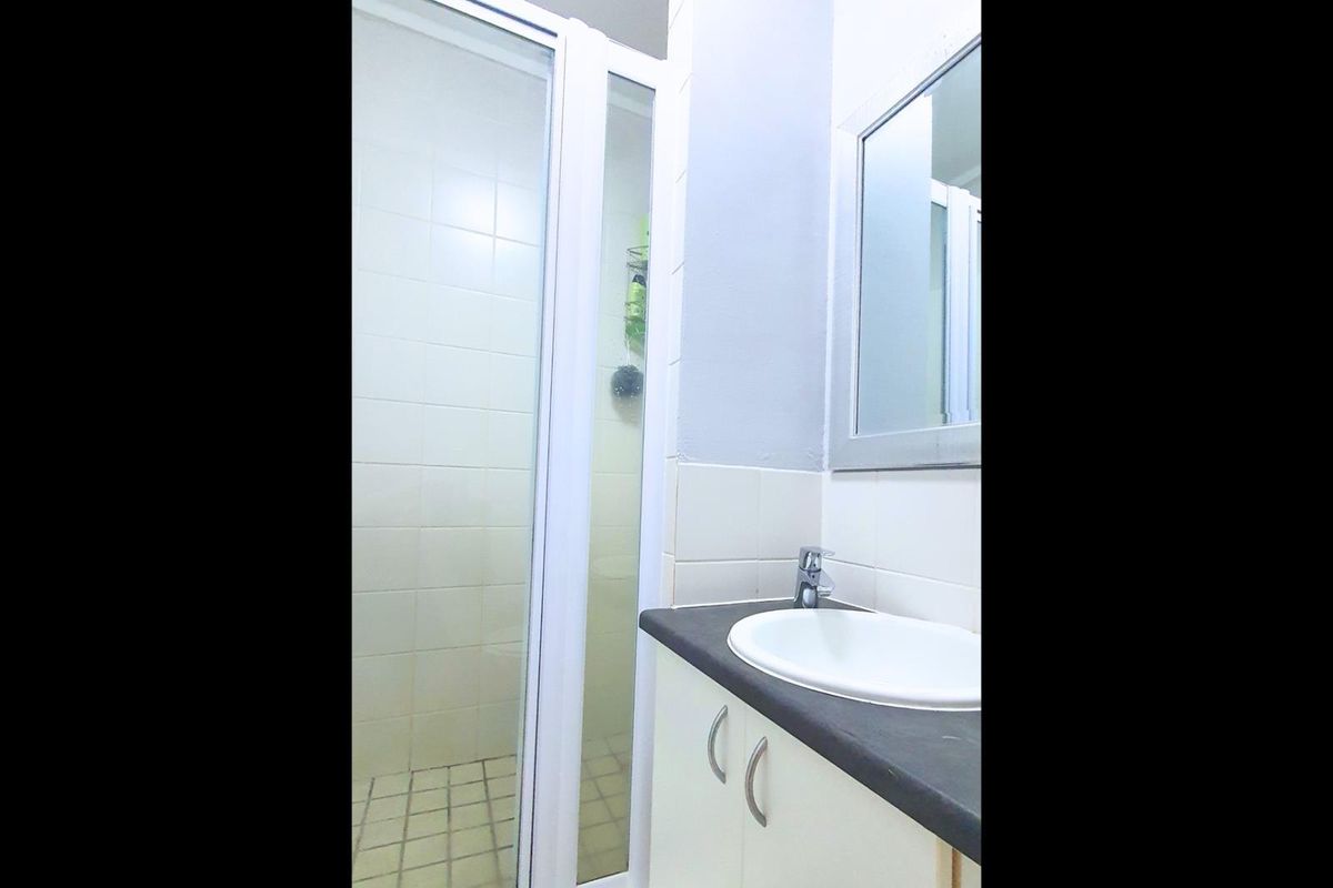 A functional bathroom featuring a shower enclosure with tiled walls and a vanity unit with a basin and wall-mounted mirror.