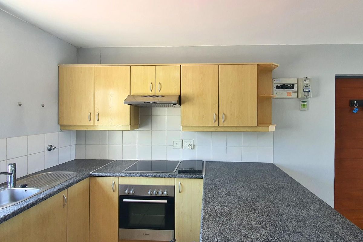 Functional kitchen featuring light wood cabinetry, granite-look countertops, built-in oven, electric hob, extractor fan, and a stainless steel sink.