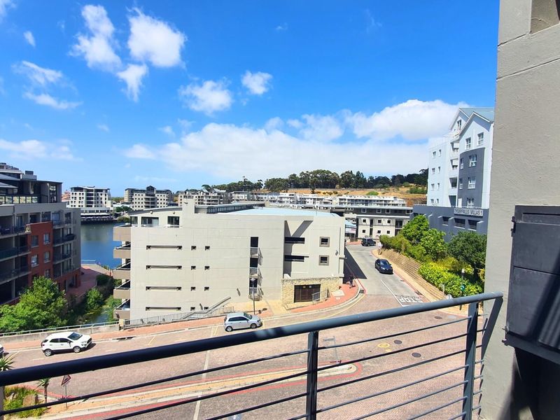 Elevated view from a balcony overlooking the surrounding apartment complex, street, and nearby water feature.