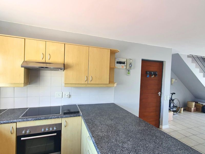 Open plan kitchen featuring light wood cabinetry, granite countertops, built-in oven, hob, and extractor fan, adjacent to a staircase and tiled living area.