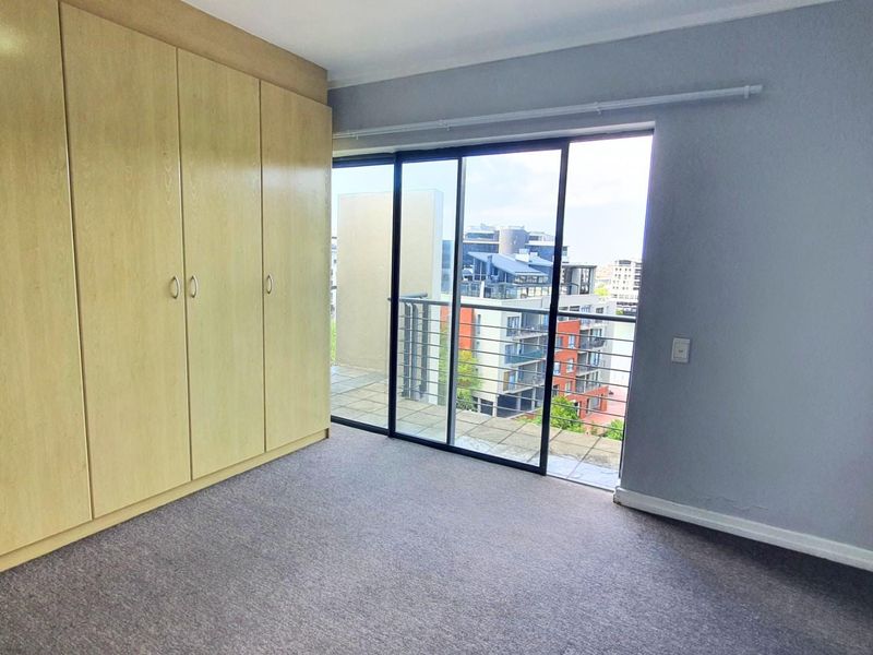 A bright bedroom featuring built-in wooden cabinetry, neutral carpeting, and large sliding glass doors opening onto a private balcony with urban views.