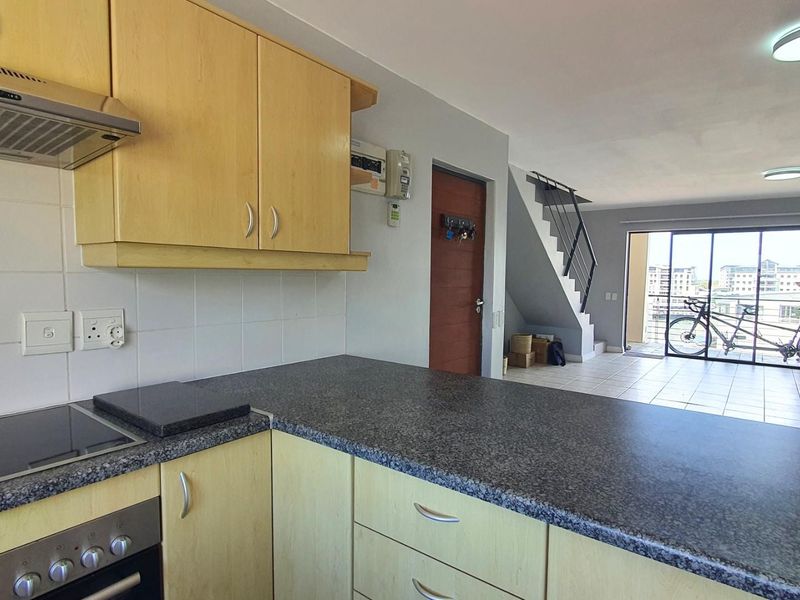 Open-plan kitchen featuring light wood cabinetry, granite-look countertops, and integrated oven with extractor fan, flowing into a spacious living area with staircase.