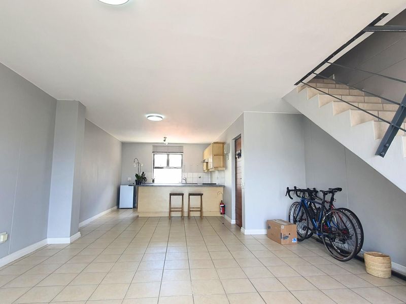 Open plan living area featuring tiled flooring, a kitchen with built-in cabinetry, and an internal staircase with a metal railing.