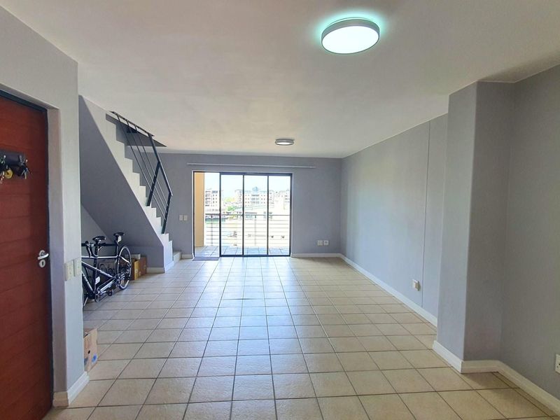 Open plan living area featuring tiled flooring, a staircase with metal railing, and sliding glass doors leading to an outdoor balcony.
