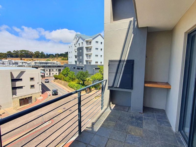 A covered balcony featuring slate tile flooring, a built-in braai, and metal railings, offering an elevated view of the surrounding residential complex and street.
