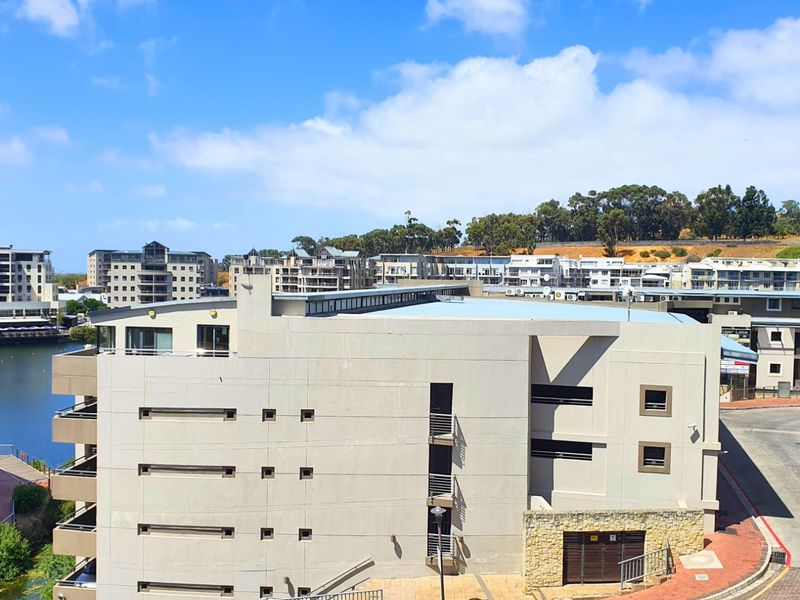 An elevated aerial view of the apartment complex, showcasing the building exterior, surrounding neighborhood, and nearby water feature.