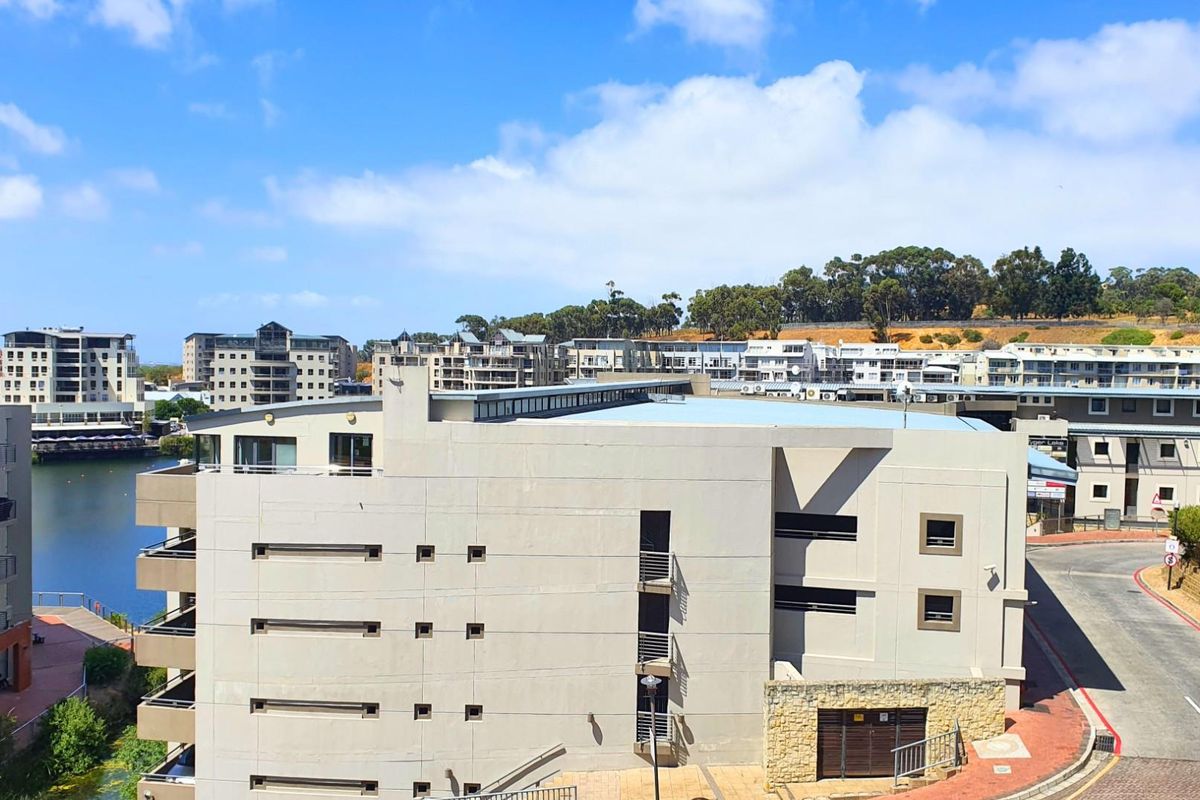 An elevated aerial view of the apartment complex, showcasing the building exterior, surrounding neighborhood, and nearby water feature.