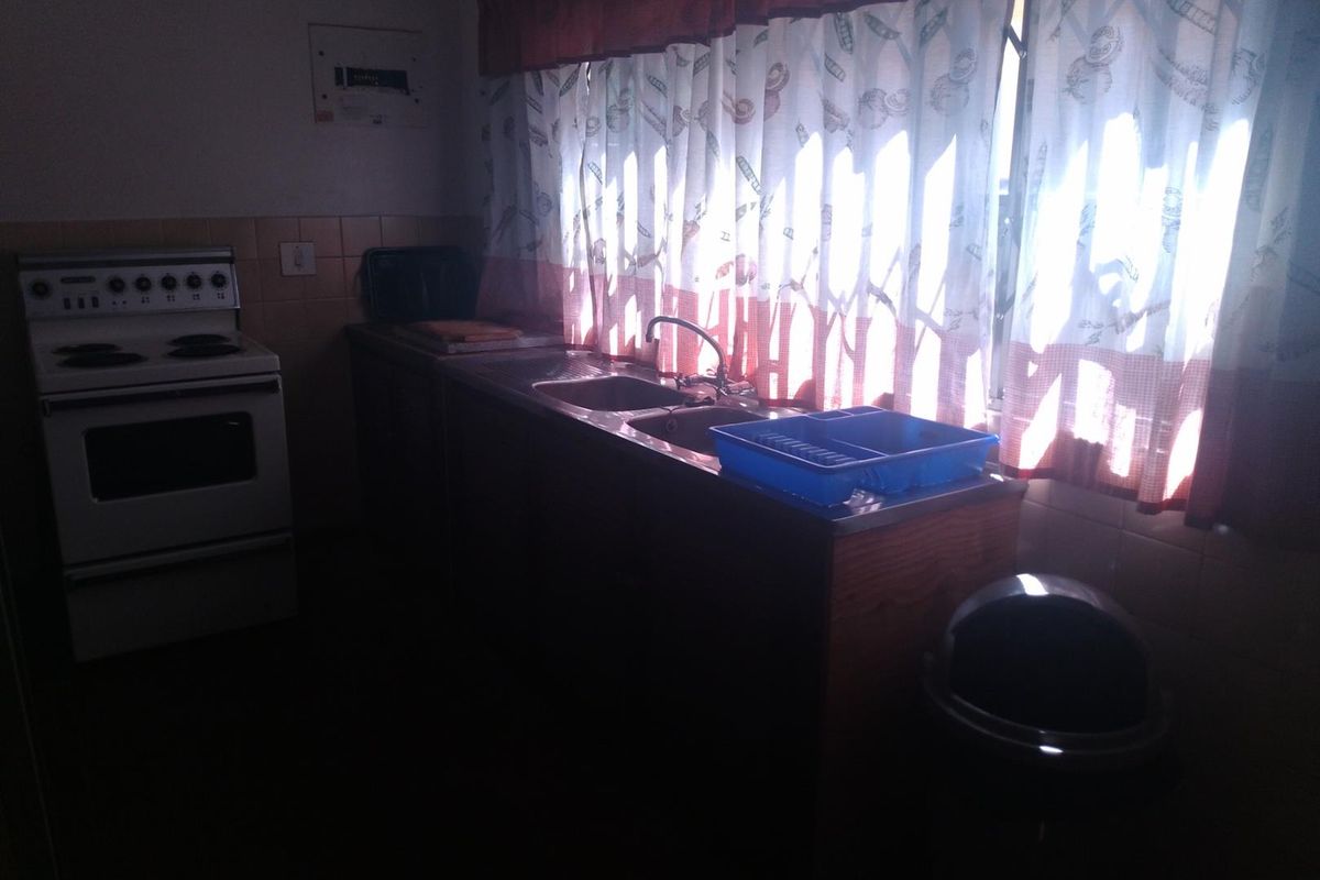 A functional kitchen featuring a freestanding stove, double bowl sink, and tiled splashback, requiring improved lighting to showcase the space effectively.