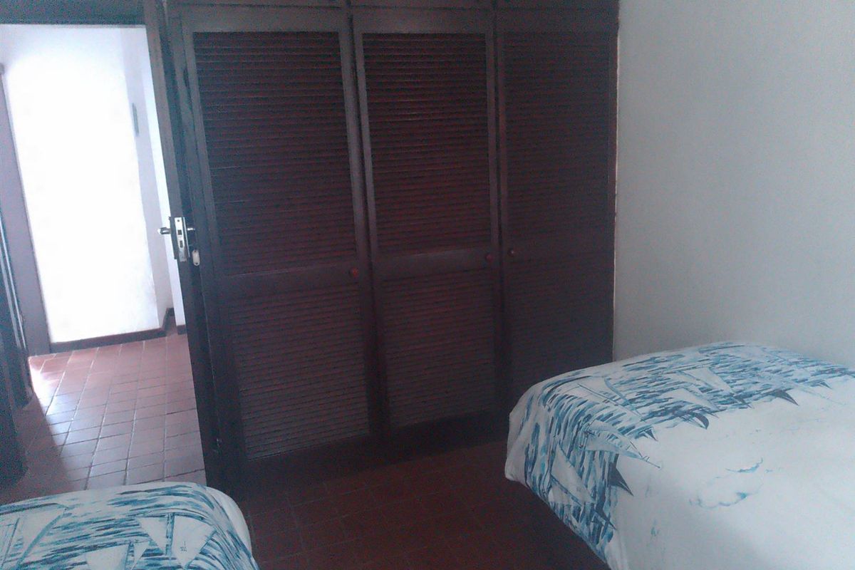 A bedroom featuring dark wood built-in cupboards with louvered doors and traditional tiled flooring.