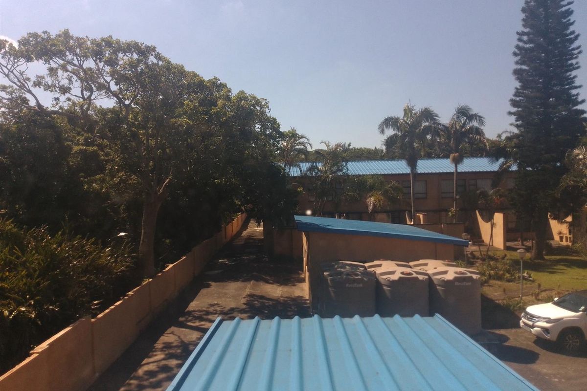 An elevated view of the rear exterior area featuring a paved driveway, boundary wall, and multiple water storage tanks adjacent to the building.