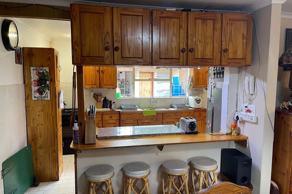 A dated kitchen featuring wooden cabinetry, a breakfast bar counter, and a pass-through window connecting to the adjacent living area.