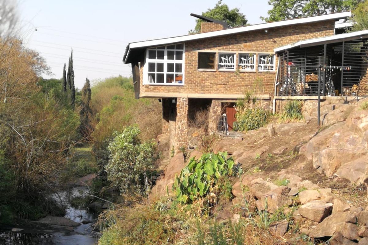 A rustic brick farmhouse exterior featuring a cantilevered design overlooking a natural stream and rocky landscape.