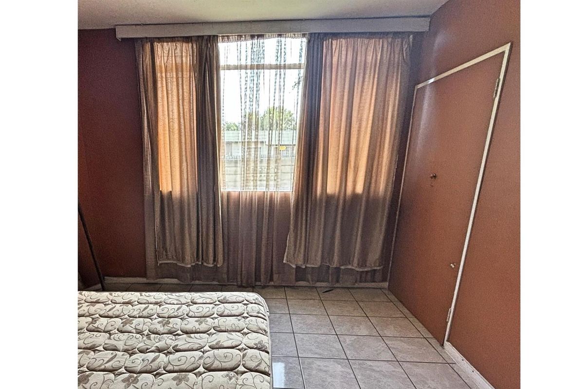 A bedroom featuring tiled flooring and a window with curtains, providing a functional space with potential for cosmetic updates.