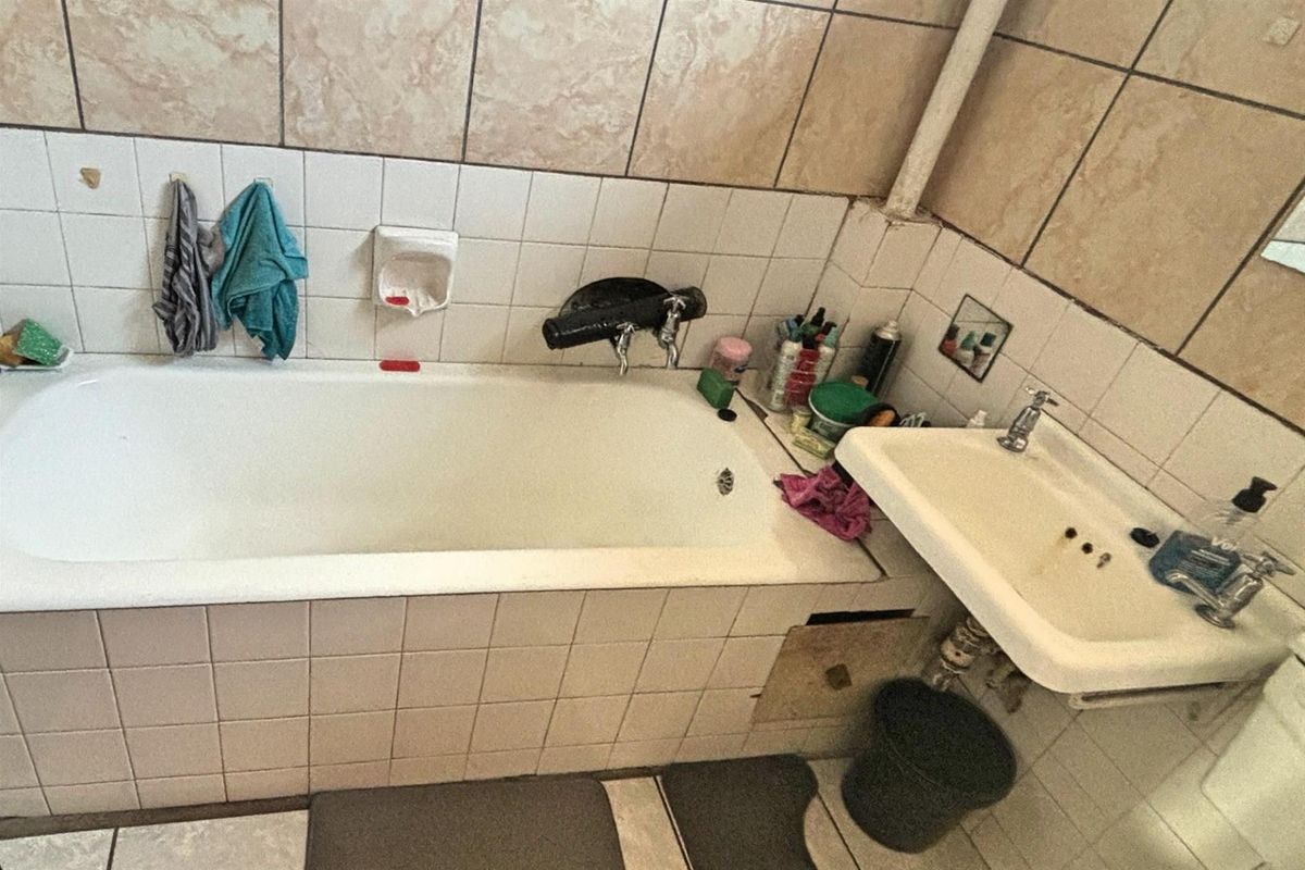 A dated bathroom featuring a tiled bathtub surround, wall-mounted basin, and ceramic wall tiling throughout.