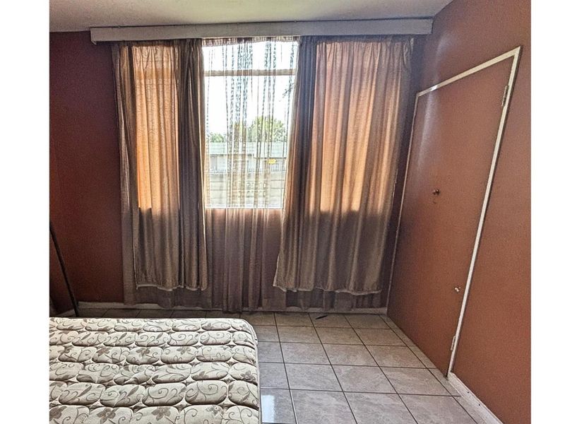 A bedroom featuring tiled flooring and a window with curtains, providing a functional space with potential for cosmetic updates.