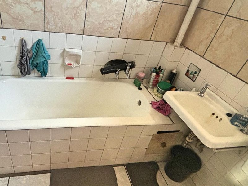 A dated bathroom featuring a tiled bathtub surround, wall-mounted basin, and ceramic wall tiling throughout.