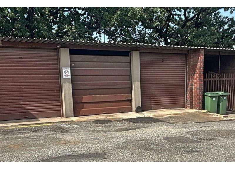 A row of three garage units featuring brown roller shutter doors and brick pillar construction, situated in a paved parking area.