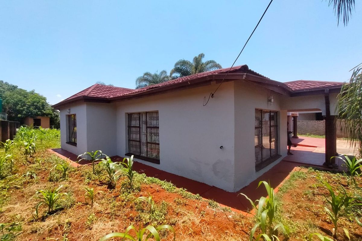 Exterior view of the house featuring a tiled roof, security bars on windows, and a surrounding garden area.