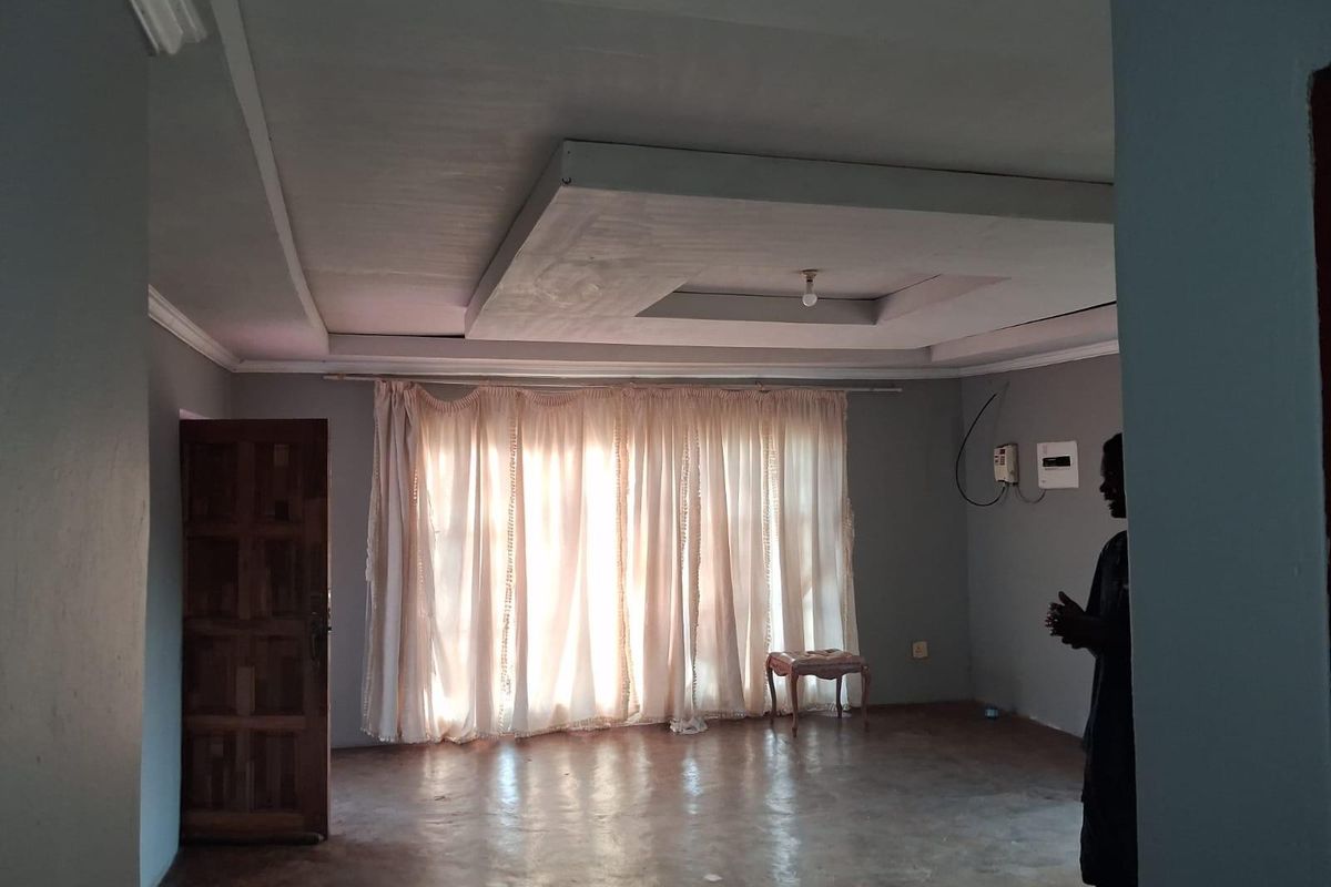 A spacious living room featuring a tray ceiling design, solid wood door, and large window with curtain fixtures.