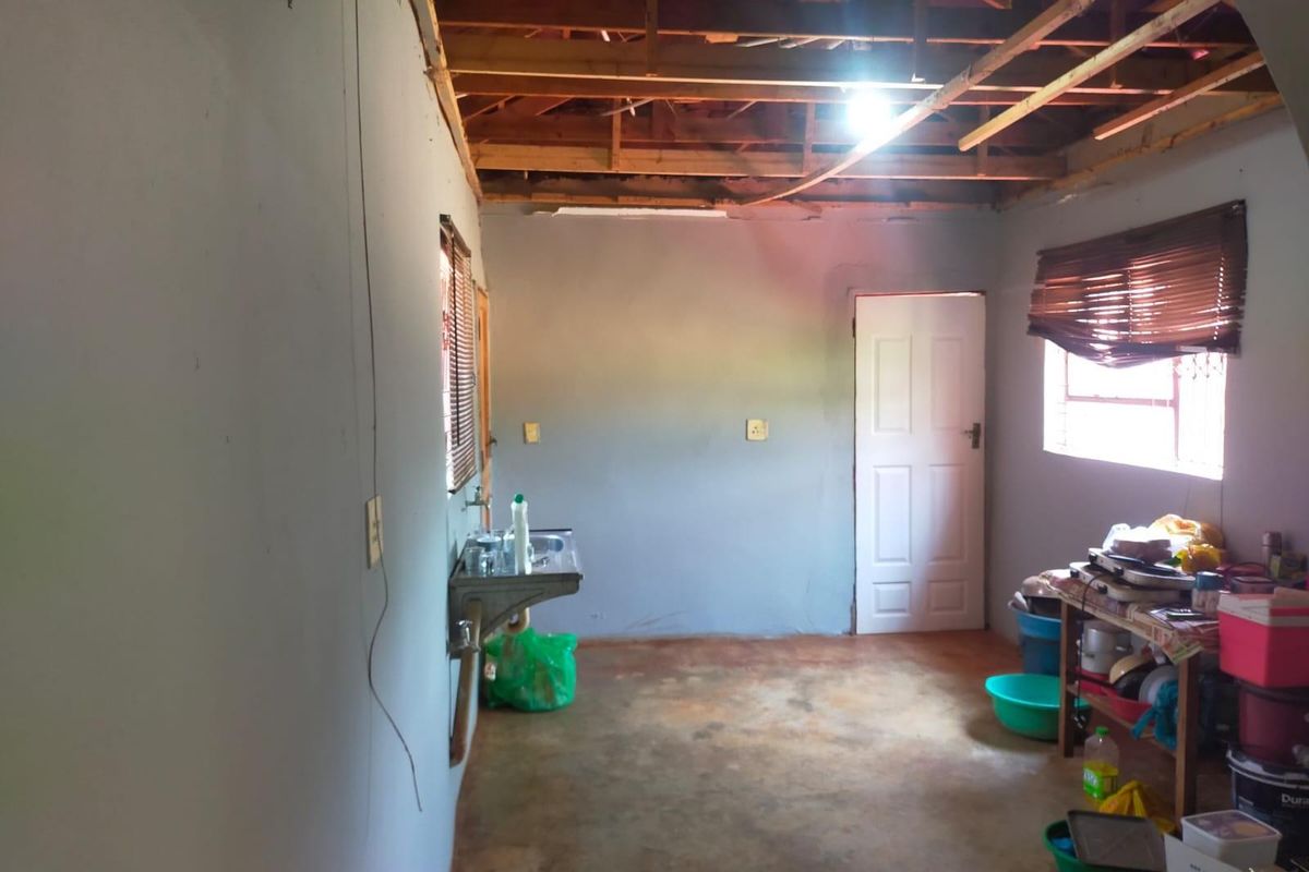 An unfinished interior space featuring exposed roof trusses, concrete flooring, and a basic wall-mounted sink, offering potential for renovation and custom finishing.