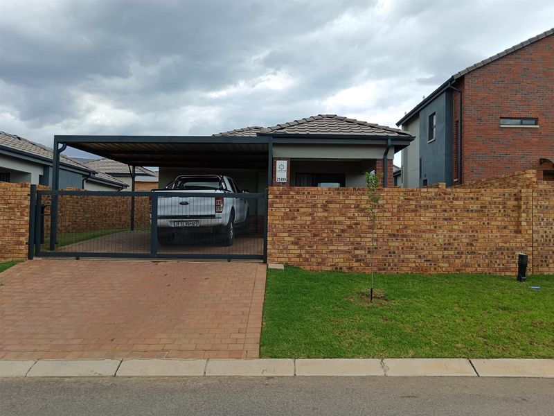 Front elevation of a modern house featuring a brick boundary wall, paved driveway, and a covered carport area.