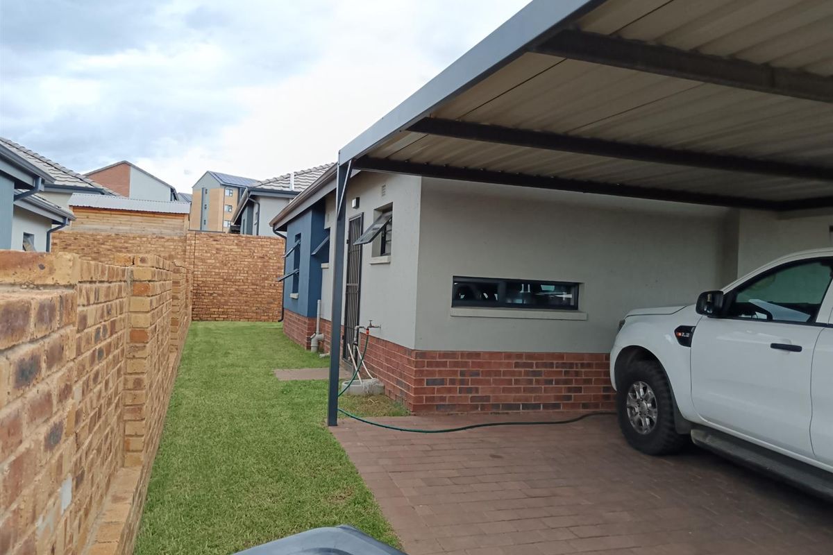 Side view of the property featuring a paved driveway with a carport, a small lawn area, and a brick boundary wall.