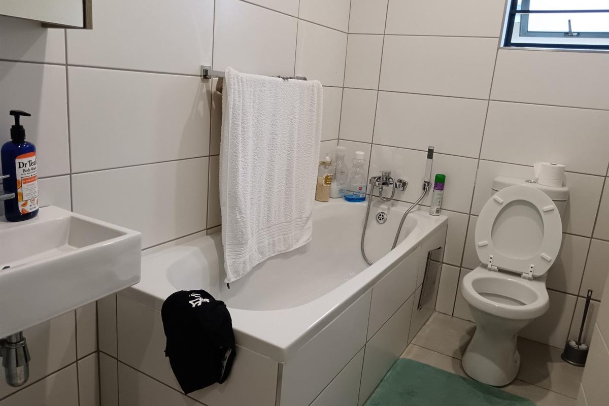 A functional bathroom featuring white wall tiles, a bathtub with a handheld shower attachment, a wall-mounted basin, and a standard toilet.