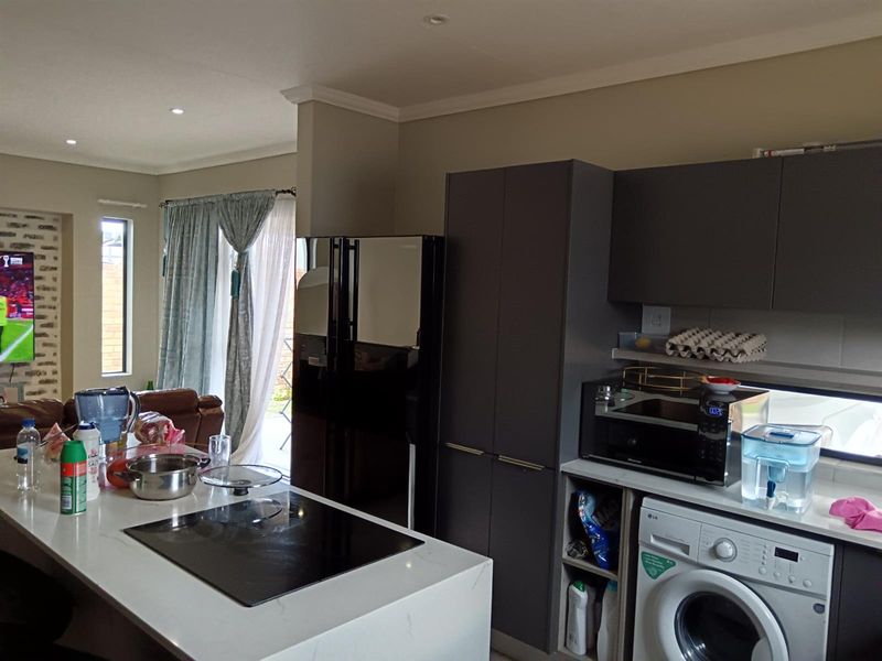 Modern open-plan kitchen featuring a central island with induction cooktop, sleek dark cabinetry, and integrated laundry appliances, flowing into the adjacent living area.