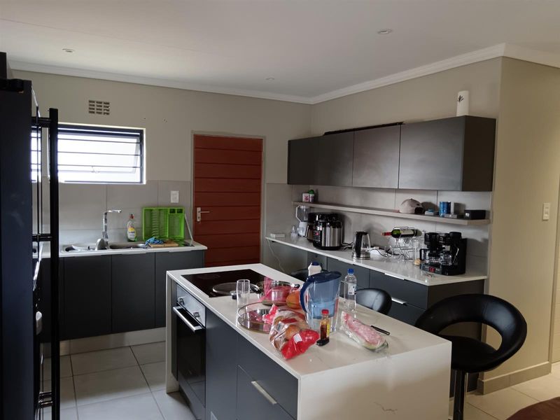 Modern kitchen featuring a central island with built-in cooktop and oven, stone countertops, ample cabinetry, and a tiled splashback.