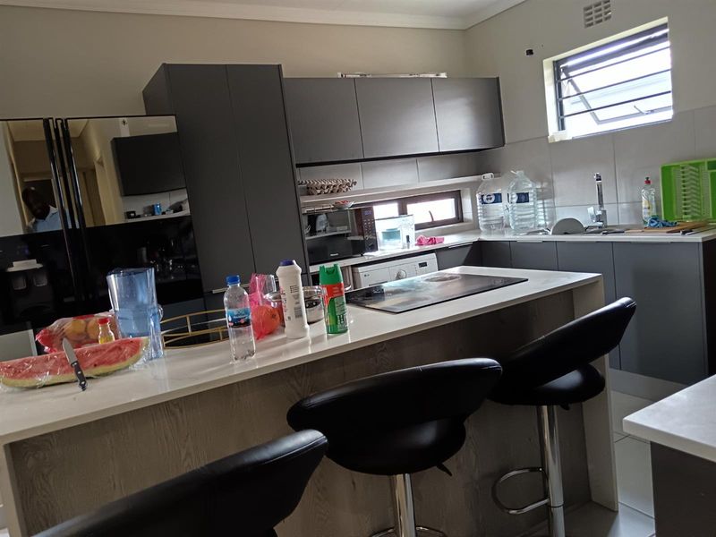 Modern kitchen featuring dark grey cabinetry, a central island with a stone countertop, integrated hob, and a tiled splashback with a functional window.