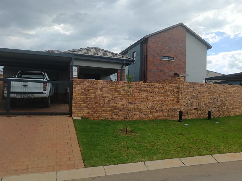 Front exterior view of a modern house featuring a brick boundary wall, paved driveway, and a covered carport area.