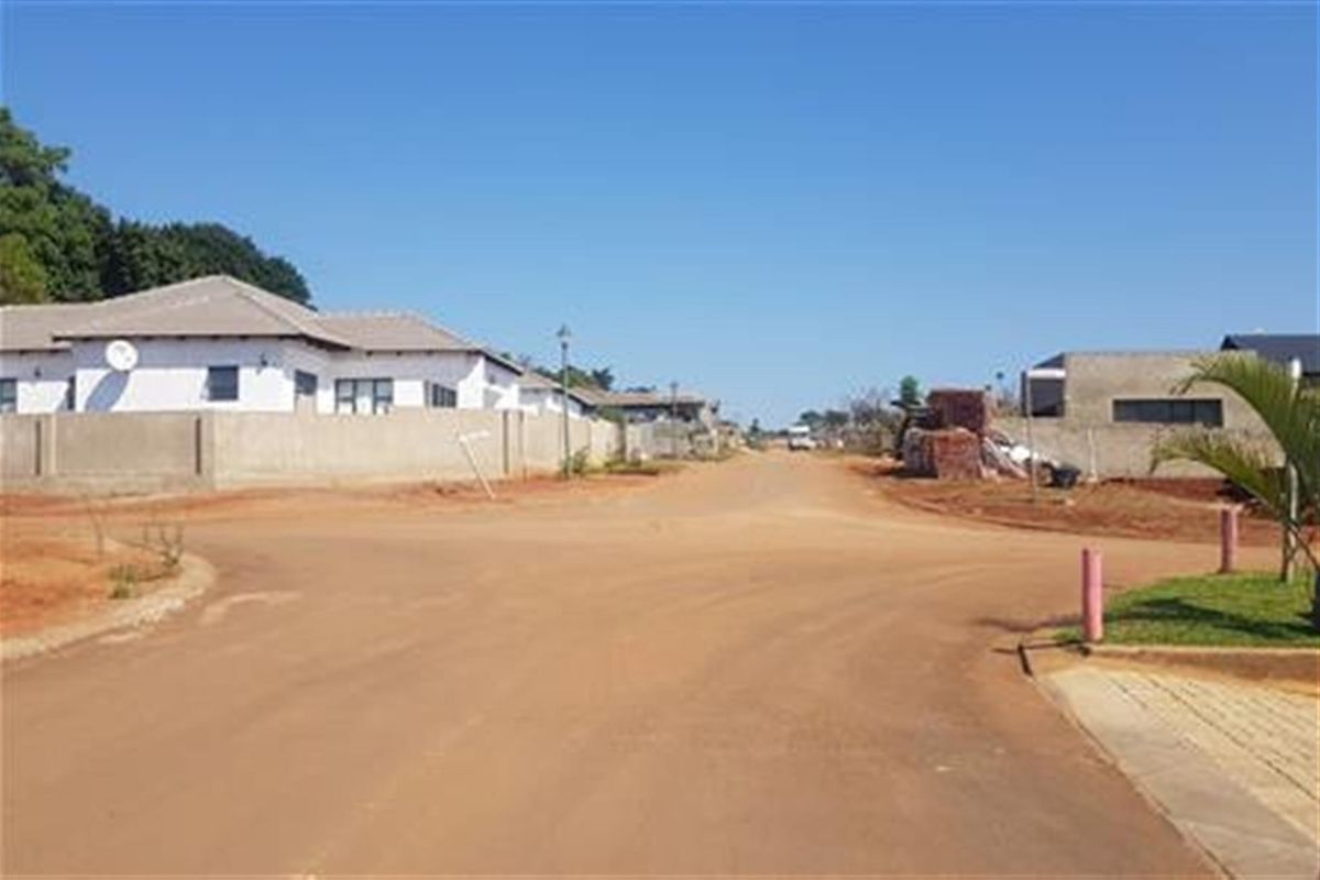 A view of a residential street in a developing estate, featuring surrounding residential properties and unpaved road infrastructure.