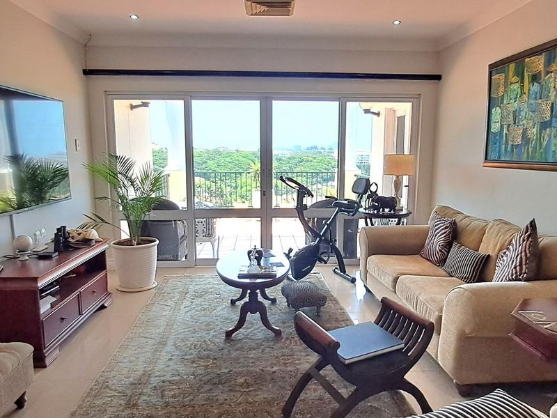 A comfortable living room featuring recessed ceiling lighting, tiled flooring, and large sliding glass doors that open onto a private balcony with scenic views.