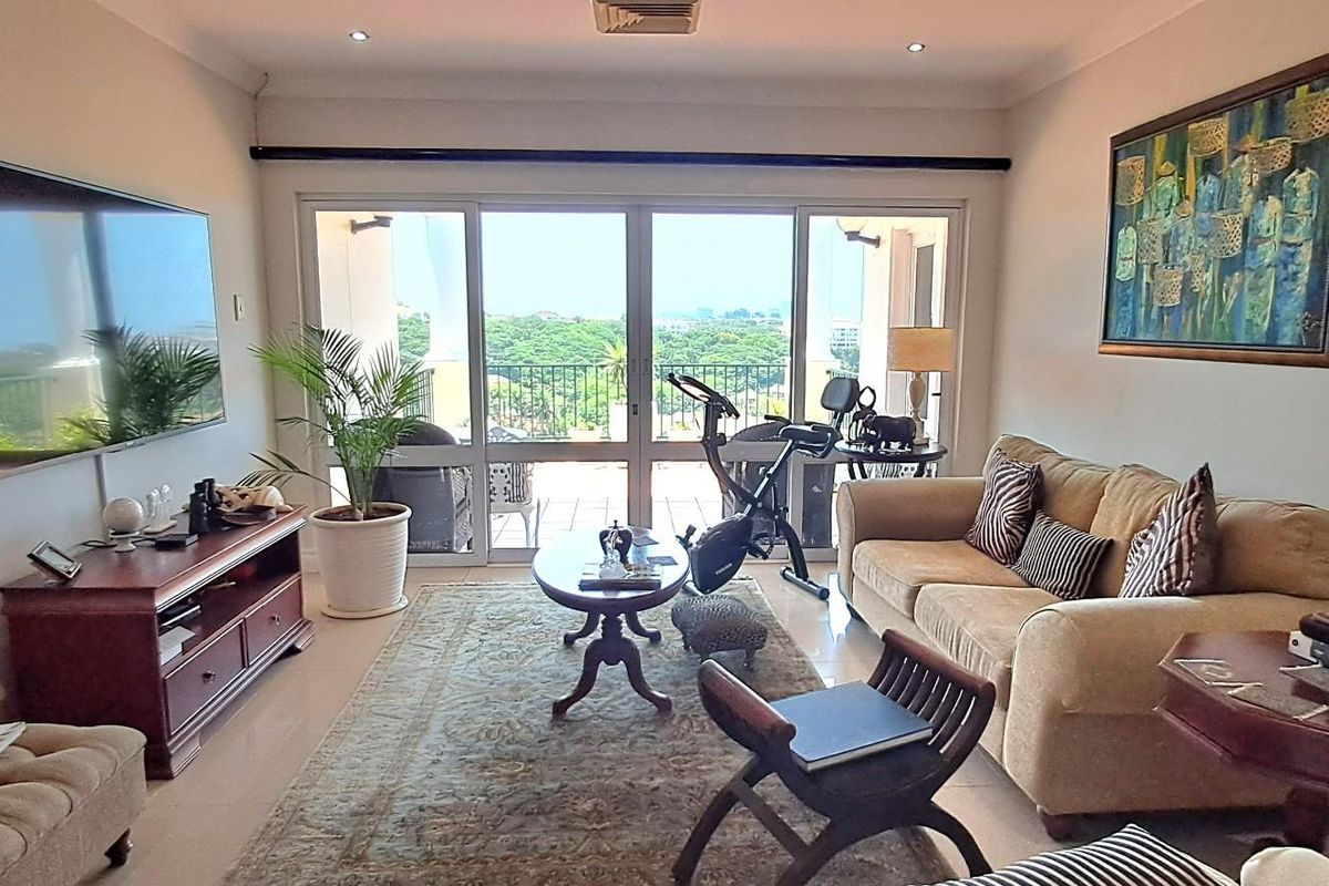 A comfortable living room featuring recessed ceiling lighting, tiled flooring, and large sliding glass doors that open onto a private balcony with scenic views.
