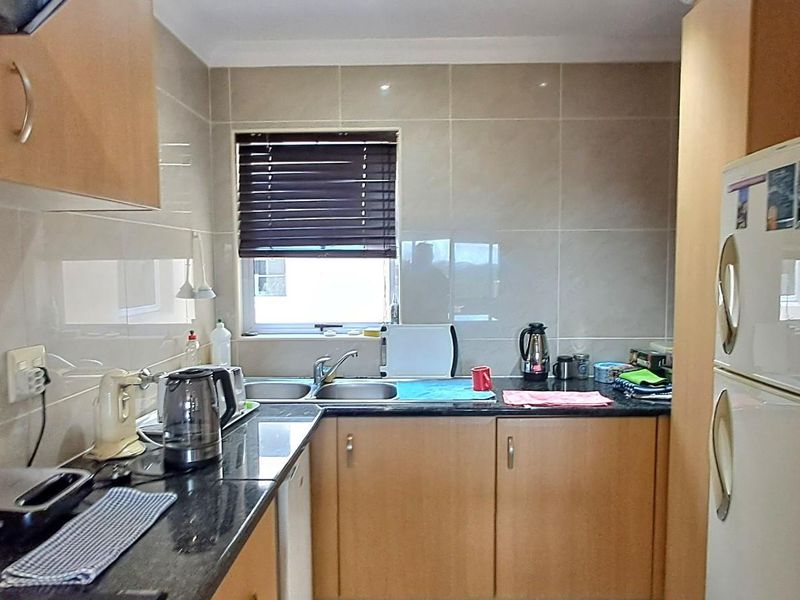 A functional kitchen featuring light wood cabinetry, dark granite countertops, tiled splashbacks, and a double stainless steel sink.