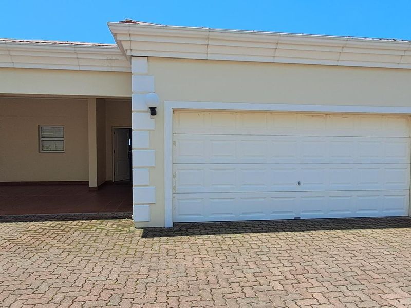 Exterior view of the apartment complex featuring a paved driveway, covered parking area, and multiple garage doors with neutral facade finishes.
